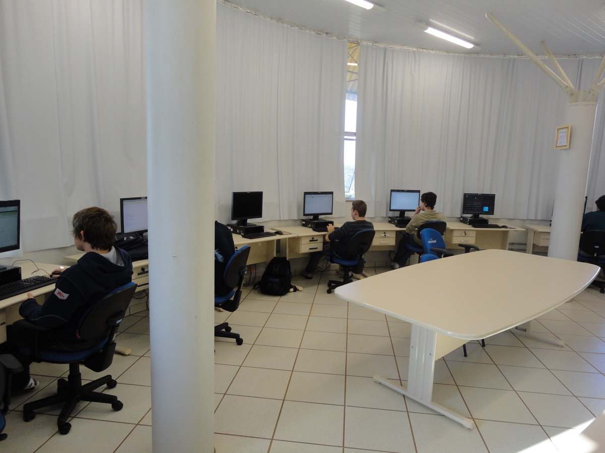 Visão ampla da sala do CRS com residentes nas estações de trabalho e mesa de reuniões ao centro.